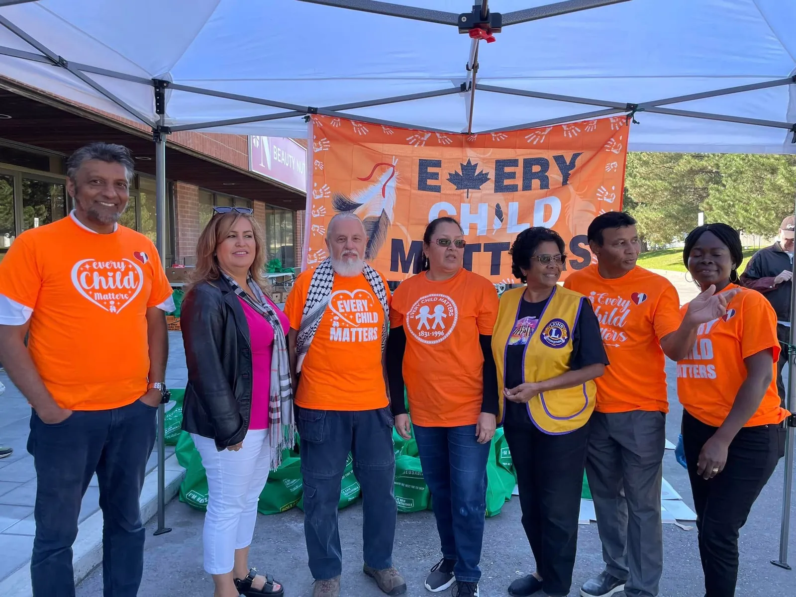 One Love volunteers in orange Every Child Matters shirts under a tent